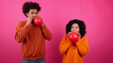 Aşklarını kutlarken gülümseyen çok ırklı neşeli bir çift. Genç, Afro-Amerikan karı ve koca kalp şeklinde balonlar üflüyorlar. Yüksek kalite 4k görüntü