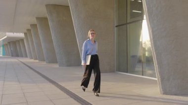 Modern şehir manzarasında, başarılı bir kadın elinde dizüstü bilgisayarla, önemli bir hedefe doğru giderken kendine has tarzını ve kararlılığını sergiliyor.