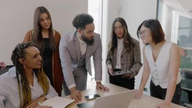 Modern ve şık bir ofis ortamında, çeşitli uzmanlar bir dizüstü bilgisayarın etrafında düşünceli ve işbirlikçi bir tartışma içinde, yenilikçi fikirler ve stratejiler paylaşıyorlar.