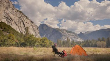 Yosemite Ulusal Parkı 'ndaki pitoresk bir kamp sahnesinde muhteşem dağların arasında canlı turuncu bir çadır var. Yürüyüş meraklıları ve doğa aşıkları için mükemmel.