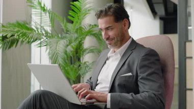 Canlı yeşilliği olan modern bir ofiste, kendini işine adamış bir işadamı laptopuna odaklanıyor ve özenle daktilo ediyor, profesyonel hedefleri doğrultusunda çalışırken bağlılığını ve konsantrasyonunu gösteriyor.