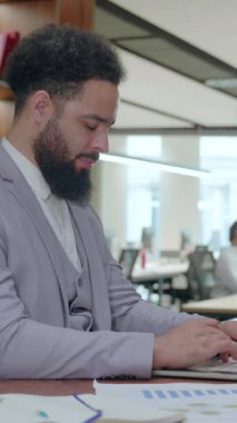 Başarılı bir Afrikalı Amerikalı işadamı modern bir dizüstü bilgisayarın başında şık bir iş yerinde oturuyor ve günümüz dinamik işgücünün üretkenliğini ve profesyonelliğini somutlaştırıyor.