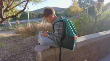 Genç çocuk, rahatlama, rahatlama ve neşe dolu keyifli bir deneyim için modern oyunu günışığıyla harmanlarken, telefonun yanında ustalıkla doğanın tadını çıkartıyor.