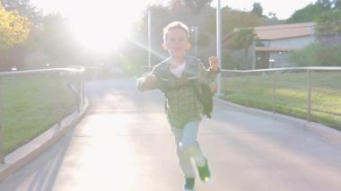 Gerçekten neşeli bir çocuk, renkli bir sırt çantası takıyor, özgürce ve büyük bir coşkuyla güneşli bir parkta koşuyor, saf macera ruhunu ve çocukluk heyecanının özünü somutlaştırıyor.