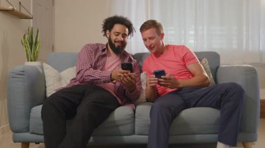 Two close friends sit on a cozy couch, absorbed in their smartphones, sharing laughs and stories, creating unforgettable memories in a warm living space while enjoying modern technologys benefits