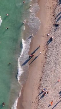 Miami Sahili 'nin büyüleyici cazibesini gösteren güzel bir hava fotoğrafı canlı turkuaz sularını aydınlatıyor ve güneşli güneşin altında ideal tatilin tadını çıkaran sayısız güneşli banyocu.