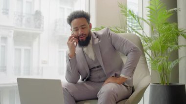 Yeşilliklerle dolu canlı ve iyi ışıklandırılmış bir çalışma alanında, takım elbiseli Afrikalı Amerikalı bir işadamı aynı anda bir telefon görüşmesiyle meşgul olurken aynı zamanda dizüstü bilgisayarı üzerinde çalışıyor.