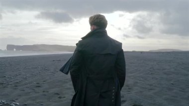 Reynisfjara 'nın güney kıyısındaki kara kumsalda yürüyen genç adam, nefes kesen manzaralar ve bu eşsiz varış yerinin güzelliğini arttıran dramatik gökyüzü ile çevrili.