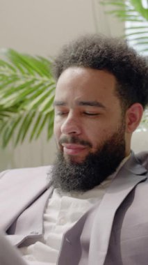 Modern ofis, keskin giyimli bir Afrikalı Amerikalı işadamı verimli yeşillikler arasında akıllı telefonuyla çalışıyor, yaratıcılığını, motivasyonunu, profesyonel çevredeki verimliliğini arttırıyor.