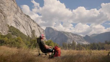 Yosemite Ulusal Parkı 'nda çekilen bu huzurlu anda, bir sırt çantasının çevresinin olağanüstü manzarasından ve deneyimlerinden keyif aldığı doğanın çarpıcı güzelliğini görüyoruz.