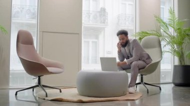 Afrika kökenli Amerikalı işadamı, atmosferi geliştiren şık mobilyalar ve canlı bitkilerle çevrili modern bir ofis veya modaya uygun bir çalışma alanında çalışmalarına odaklanmış durumda.