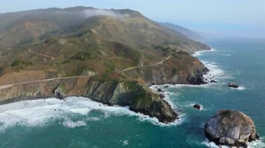 Big Sur 'un hava görüntüsü, 1. Otoyol ve çarpıcı Kaliforniya kıyı şeridi boyunca giden bir arabayı cezbediyor. Dalgalar ve çeşitli manzaralarda nefes kesici güzellikler sergiliyor.