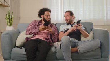 İki arkadaş, rahat bir koltukta akıllı telefonlarını kullanırken neşeli ve neşeli bir anı paylaşıyorlar. Böylece günlük yaşamlarındaki teknoloji ve etkileşimlerini güçlendiriyorlar.