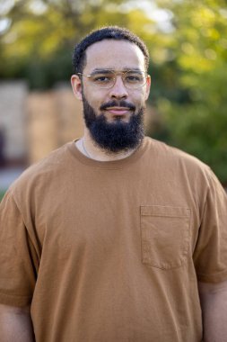 Şık gözlükler takan Afro-Amerikalı bir adam, doğal karizmasını ve varlığını gerçekten arttıran güzel ve sakin bir ortamda, sakin ve sakin bir şekilde dışarıda duruyor.