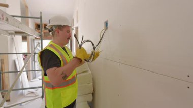 Kablolarla çalışan inşaatçı, detaylı bir ev yenileme planını uygulamak için çeşitli araçlar kullanıyor. Parlak güvenlik kaskları profesyonelliklerini ve güvenliğe olan bağlılıklarını vurguluyor