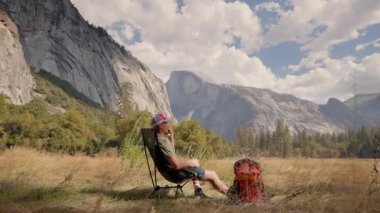 Bir adam bir sandalyede rahatça dinlenmek için bir dakikasını ayırır, yanında sırt çantasıyla dinlenir, hepsi Yosemites 'in nefes kesici ve görkemli manzarasına karşı hazırdır.