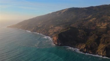 Büyüleyici hava görüntüleri, Kaliforniya 'nın ünlü Karayolu 1 boyunca uzanan Big Sur' un nefes kesici manzarasını sergiliyor. Gün batımı yaklaşırken engebeli ve dramatik kıyı şeridini sıcak renklerle yakalıyor.