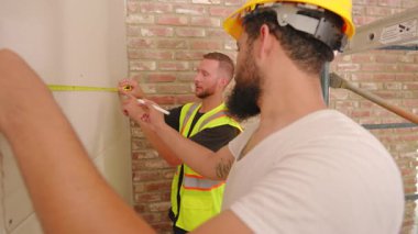 Çeşitli geçmişlerden yetenekli müteahhitlerden oluşan çeşitli ekipler, yeni bir ev yenileme projesi için özenle ve titizlikle ölçüp planlama yaparak, bir inşaat sahasında etkin bir şekilde iş birliği yapıyorlar.