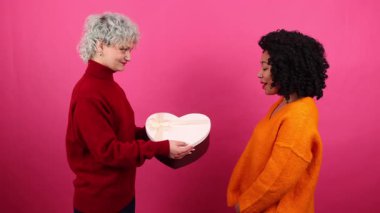 LGBT çifti pembe izole edilmiş arka planda birbirlerine hediye verirken yakın çekim. Romantik duygularını ifade eden çekici kadınlar. Yüksek kalite 4k görüntü