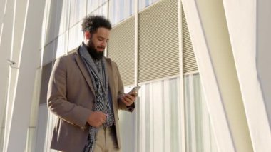 Şık bir binanın dışındaki telefon görüşmesinde şık giyinmiş işadamı, güven ve kararlılığın bir örneği olarak, başarılı bir şirket kariyeri ve başarıya olan bağlılığını vurguluyor.