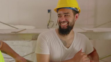 Kalabalık bir inşaat sahasında çeşitli bir ekiple birlikte çalışarak, ev yenilemesindeki takım çalışmasının ve yaratıcılığın önemini vurgulayan neşeli inşaatçılar mutlulukla ışıldıyorlar.