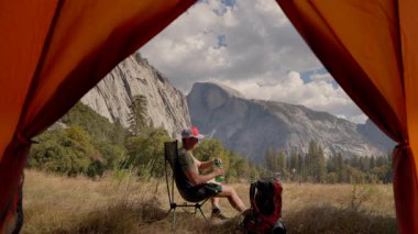 Yosemite Milli Parkı 'nın nefes kesici manzarasından hoşlanan erkek yürüyüşçü, sandalyede oturuyor ve şişeden su içiyor çarpıcı manzaralı, açık hava yaşam tarzı keşif ve macera davet ediyor. 