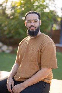 Büyüleyici bir portre, şık kahverengi gömlekli ve gözlüklü sakallı bir Afrikalı Amerikalı 'yı gösteriyor. Açık havanın dingin güzelliğinin tadını çıkarırken kendine güveni yayıyor. Hoş bir atmosfer yaratıyor.