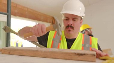 Yoğun inşaat sahası, güvenlik kaskı ve yelek giyen kendini işine adamış bir işçi, yenilikler için ustalıkla araç kullanıyor ve topluluk oluşturmada takım çalışması ve beceri çeşitliliğinin önemini vurguluyor.