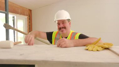 Gülümseyen inşaatçının portresi ve yoğun bir inşaat sahasında işbirliği içinde çalışmak, evleri yenilemek ve başarılı olmak için takım çalışması ve işbirliği yapmakla meşgul olmak.