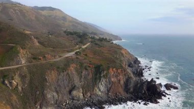 Büyük Sur, California 'daki ikonik 1 numaralı otoyol boyunca muhteşem Pasifik sahilini çeken nefes kesici hava sahnesi çarpıcı bir günbatımı altında dramatik uçurumlar ve güçlü okyanus dalgaları sergiliyor.