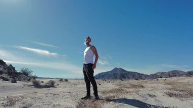 Kuru ve kurak çölün engin genişliğinde, solunum maskesi ile donatılmış yalnız bir figür, sert ve korkunç bir kıyamet sahnesinin ortasında hayatta kalma ve yalnızlığın güçlü temaları ile yankılanıyor.