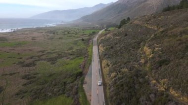 Nefes kesen hava manzarası, günbatımında Kaliforniya Big Sur sahil şeridine çarpıcı bir bakış açısı sunuyor. Dönen otoyolu kullanan araba, çevresindeki doğal manzarayı güzellikle tamamlıyor.