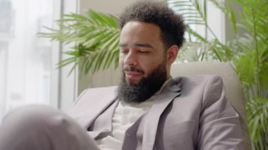 Modern ofis, keskin giyimli bir Afrikalı Amerikalı işadamı verimli yeşillikler arasında akıllı telefonuyla çalışıyor, yaratıcılığını, motivasyonunu, profesyonel çevredeki verimliliğini arttırıyor.