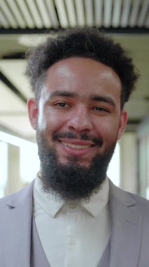 Gülümseyen bir Afro-Amerikan işadamı, işbirliği ve yaratıcılığı teşvik eden, profesyonellik ve liderlik havası yayan, stil sahibi, modern bir çalışma alanında kendine güvenerek duruyor.