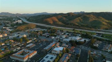 Los Angeles banliyösündeki işlek bir otobanın yanındaki canlı yeşil tepelerin çarpıcı görüntüsü, gün batımında güzelce çekilmiş, manzarayı çarpıcı renklerle aydınlatıyor.