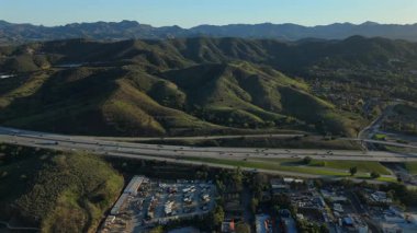 Los Angeles 'ın banliyölerinde çekilen nefes kesici insansız hava aracı görüntülerinde yemyeşil tepeler, hareketli otoban trafiği ve manzarayı sıcak tonlarda boyayan büyüleyici günbatımı ışıkları görülüyor.