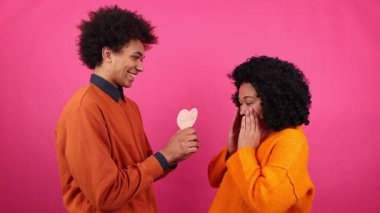 Afro-Amerikan kadın portresi şaşkın ve neşeli görünüyor. Sevgililer günü kartını kıza sunan 20 'li yaşlarda bir erkek arkadaşın yakın çekimi. Yüksek kalite 4k görüntü