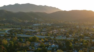 Nefes kesen hava görüntüleri, büyüleyici bir günbatımı sırasında, canlı yeşil tepeler, görkemli dağlar ve hareketli otoban trafiğini gözler önüne seren Los Angeles banliyösünü güzel bir şekilde yakalıyor.