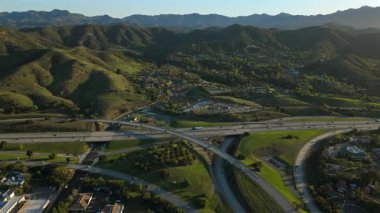 Los Angeles 'taki güzel bir banliyö bölgesinin çarpıcı hava görüntüleri. Yeşil tepeler, yoğun otoyollar ve nefes kesici bir gün batımı arka planına karşı manzaralı bir kavşak.