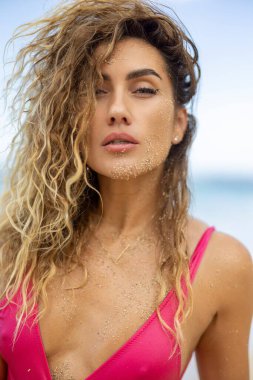 Bu resim, Hawaii sahillerinde güneşten zevk alan genç bir kadını, kendine güvenini arttıran canlı pembe bir mayo giyerken, dalgalı saçlar ve ışıltılı bir gülümseme ile, tropikal bir rahatlamayı somutlaştırırken gösteriyor.