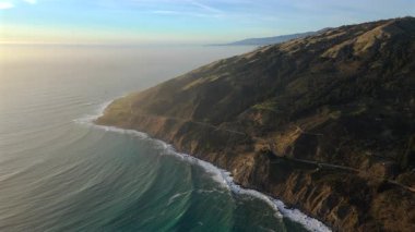 Nefes kesici hava manzarası, gün batımında ikonik 1. Otoyol boyunca uzanan ve Kaliforniya 'nın engebeli ve görkemli doğal manzarasını gözler önüne seren Big Sur' un büyüleyici güzellikteki sahil şeridini harika bir şekilde yakalıyor.