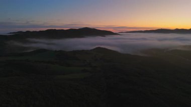 Gün batımında Malibu dağlarının nefes kesici hava manzarası. Yeşil tepeler sisle harmanlanır. Büyüleyici ve sakin bir manzara yaratır.