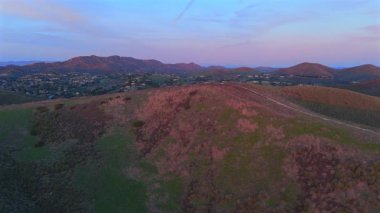 Güneş batarken yemyeşil tepelerin yumuşak bulutlarla buluştuğu görkemli Malibu dağlarının nefes kesen hava manzarasını deneyimleyin. Büyüleyici ve büyüleyici bir manzara yaratıyor.