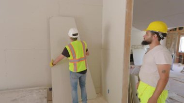 Güvenlik kaskı takan kendini adamış müteahhit takımı, inşaat sektöründe takım çalışması, kararlılık ve profesyonellik sergileyen büyük bir ev yenileme projesinde işbirliği yapıyor.