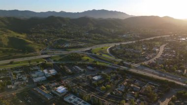Los Angeles 'ın çarpıcı hava görüntüleri banliyö manzarasını sergiliyor. Yeşil tepeler, işlek otobanlar ve muhteşem bir günbatımı sırasında manzaralı kavşaklar. Görsel deneyimi artırıyor.