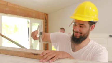 Aralarında Afro-Amerikan, İspanyol ve Kafkas işçilerin de yer aldığı çeşitli inşaatçılar, araçlar ve sergilenen takım çalışması ve işbirliği kullanarak kalabalık bir alandaki evleri memnuniyetle yeniliyorlar.