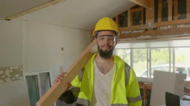 Neşeli Afro-Amerikan inşaat işçisi koruyucu giysiler içinde sağlam ahşap bir kiriş tutuyor ve inşaat sektöründe yüksek güvenlik standartları ve profesyonelliği gösteriyor.