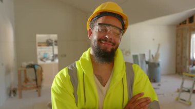 Neşeli Afro-Amerikan inşaat işçisi, parlak güvenlik teçhizatlarıyla, tamamlanmamış bir binada, projeye etkin bir şekilde katkıda bulunma isteği ve olumlu bir tutum sergiliyor.