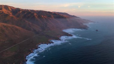 Günbatımında muhteşem Big Sur kıyılarını bir hava görüntüsü yakalıyor, 1. Otoyol 'u aydınlatıyor ve okyanus dalgalarını vurguluyor, California' nın güzel ve sakin manzaralarını somutlaştırıyor.