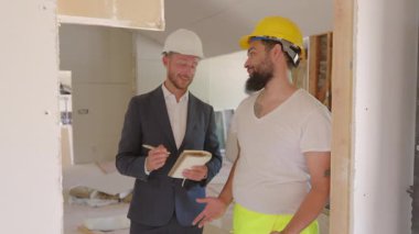 Yoğun bir yenileme sahasında, yetenekli bir inşaat işçisi projeyi gayretli bir işçiyle tartışarak, çabalarının başarıya ulaşması için etkili bir işbirliği yapıyor.